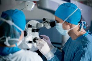 Surgeons performing an eye surgery under the microscope at the hospital - healthcare and medicine concepts