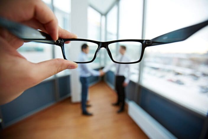 Male hands holding glasses for you to look at two businessmen shaking hands