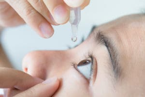 person putting eye drops in their eye