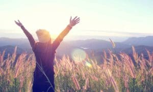 Happy Woman Enjoying Nature on grass meadow on top of mountain cliff with sunrise